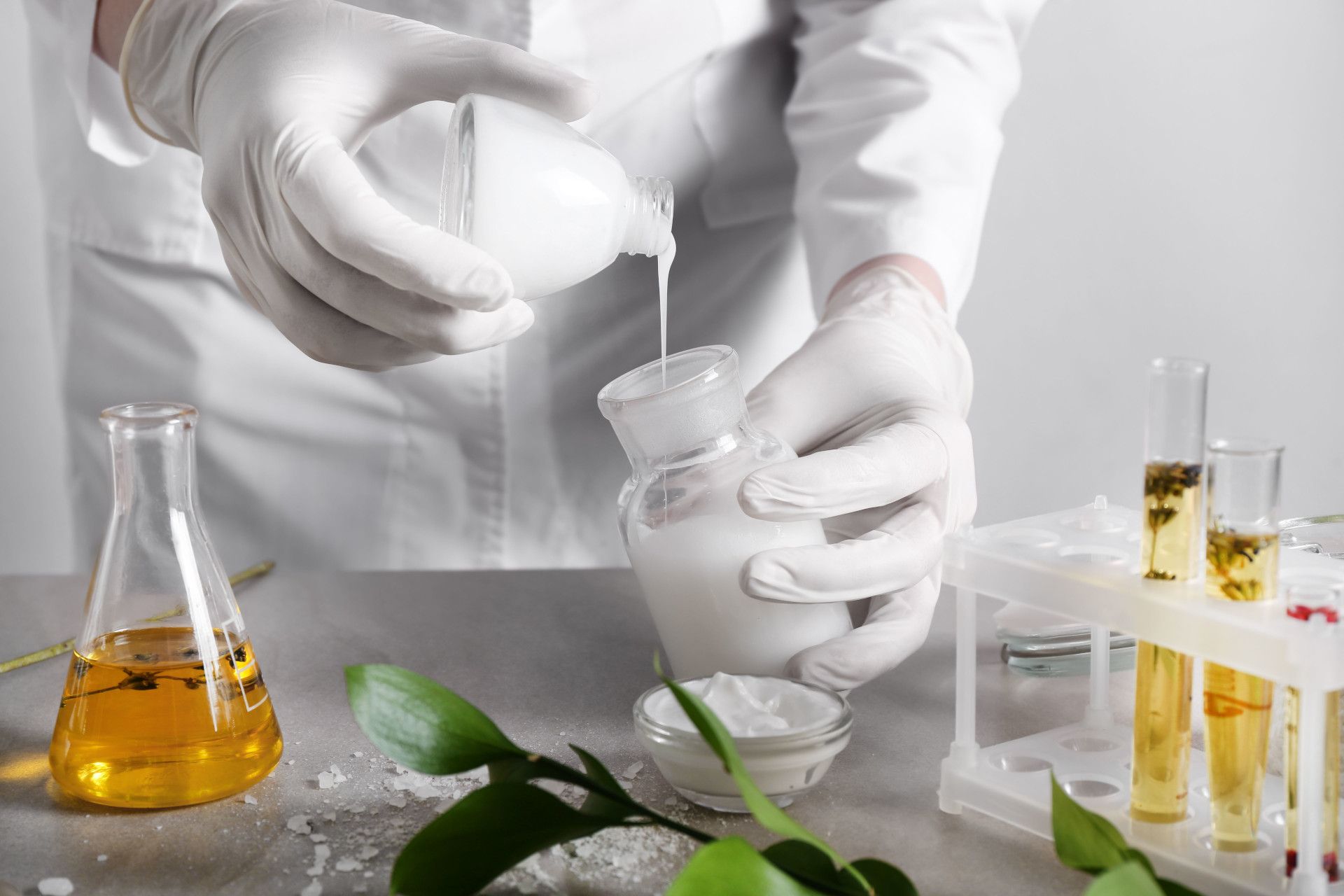 mani del tecnico di laboratorio durante la preparazione delle creme viso Ayame con prodotti naturali sul tavolo di marmo con piante e spezie