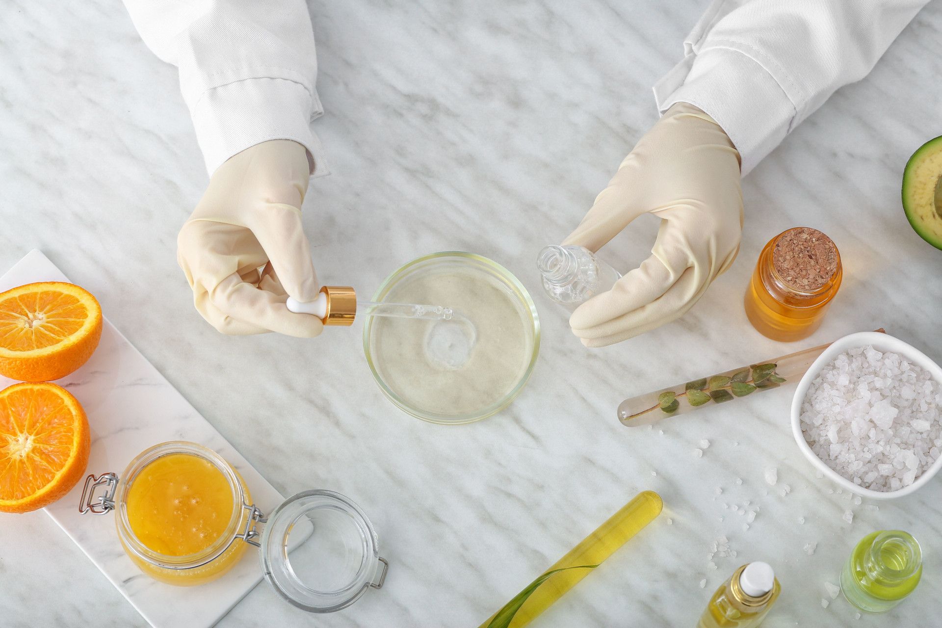 mani del tecnico di laboratorio durante la preparazione dei cosmetici Ayame con prodotti naturali sul tavolo di marmo con arance e spezie